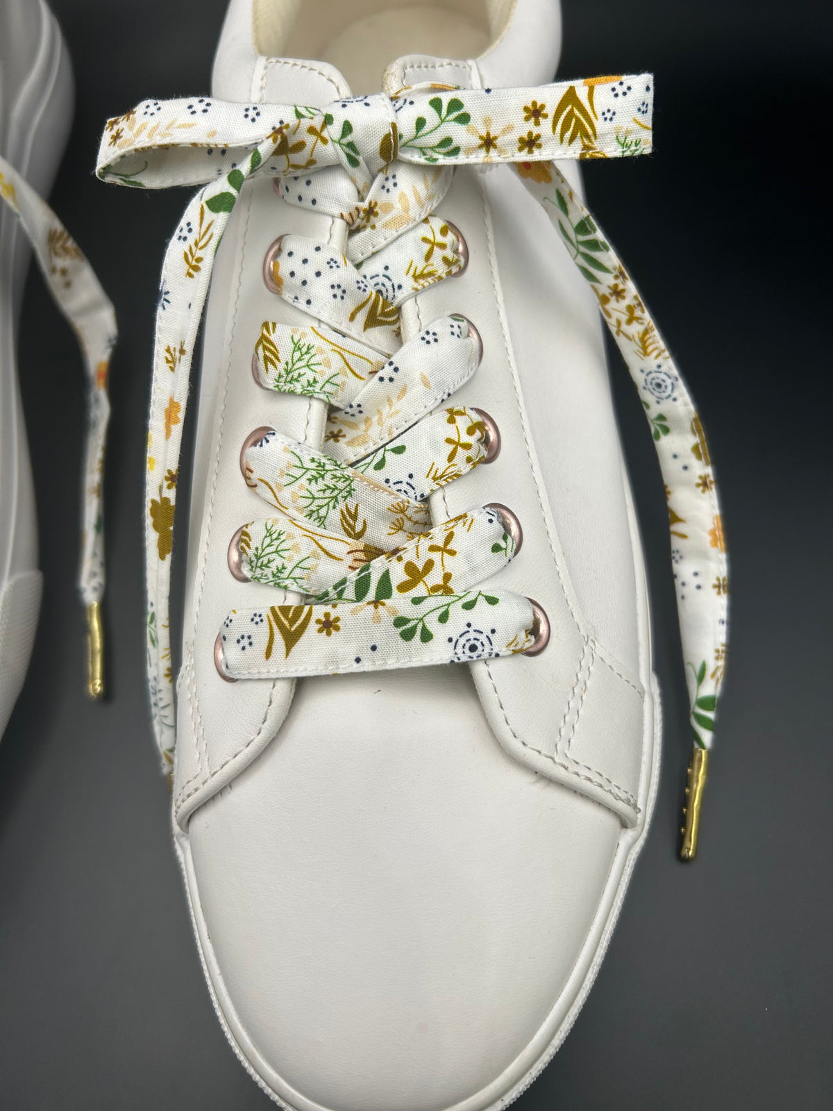 Lacets fleuris en tissu noués sur basket blanche, vue de dessus 