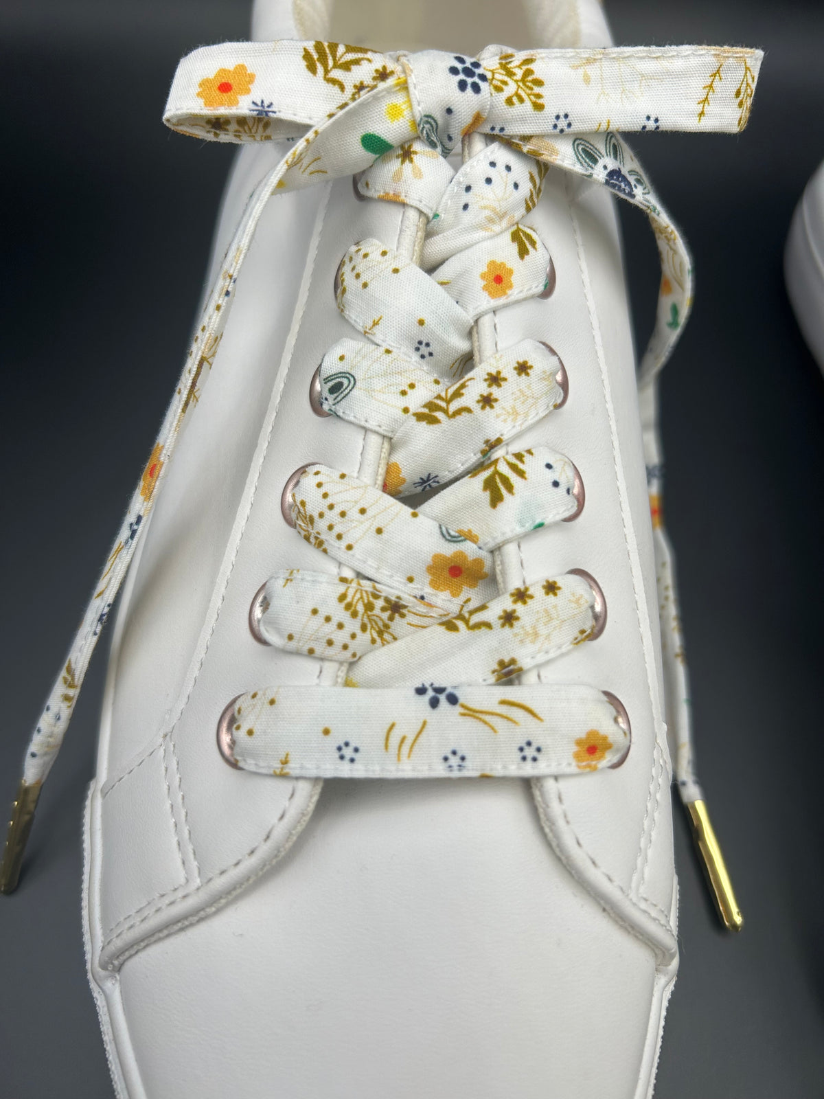 Lacets fleuris en tissu sur basket blanche, gros plan sur le laçage
