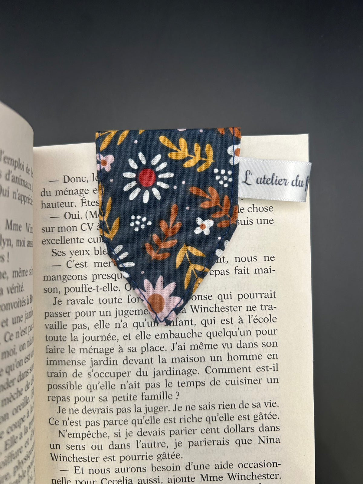 Marque-page aimanté en tissu à fleurs fixé sur une page ouverte, étiquette L'atelier du fil créatif