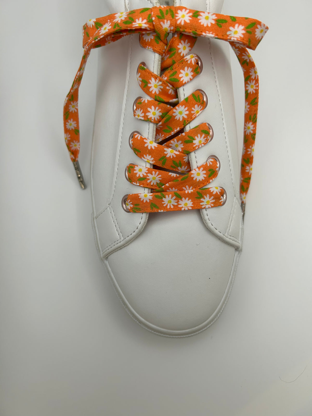  Vue de dessus d’une basket blanche aux lacets orange à marguerites, noués en boucle
