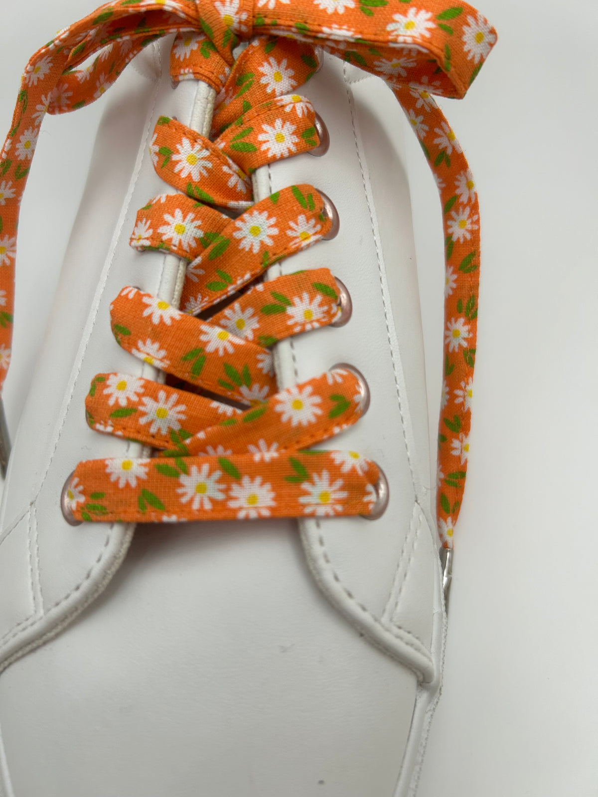 Détail des marguerites blanches et du feuillage vert sur les lacets orange d’une basket blanche