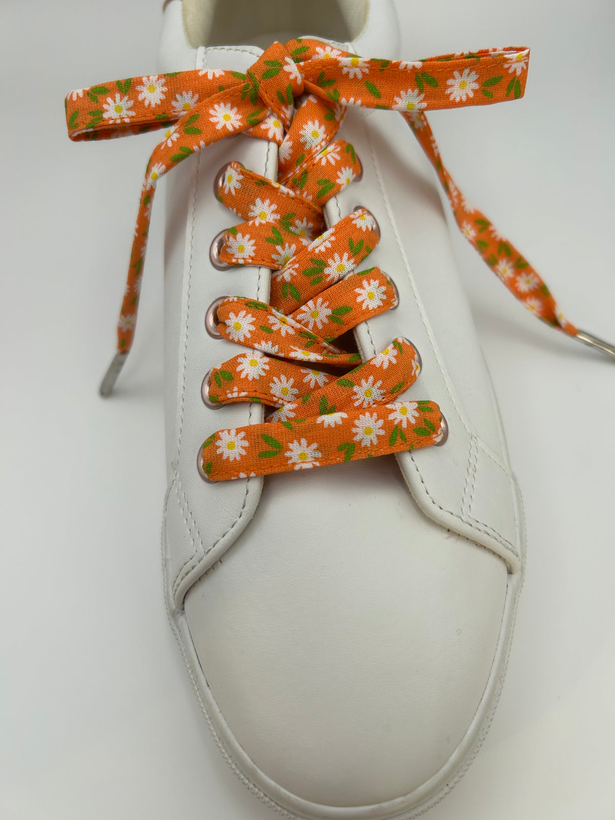 Gros plan sur le laçage et le nœud de lacets orange à marguerites blanches sur une basket blanche