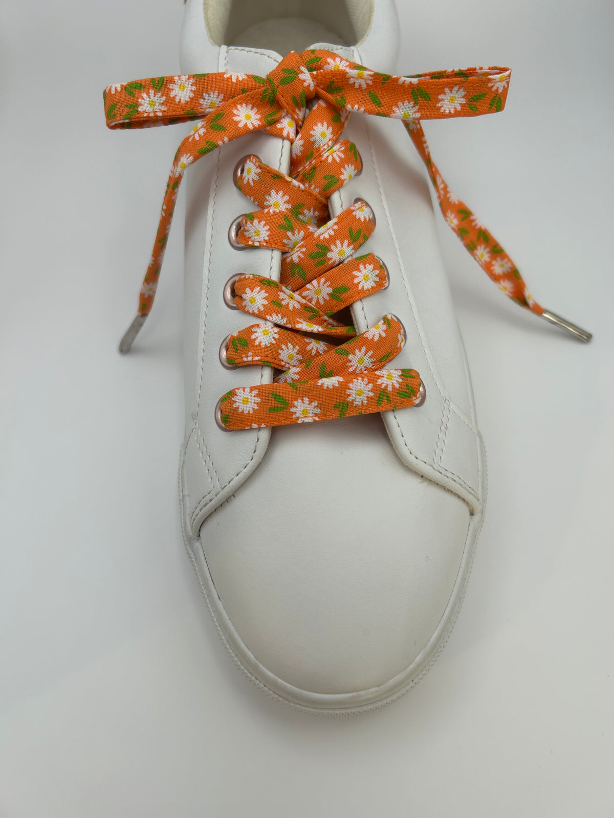 Vue de dessus d’une basket blanche avec des lacets orange à motif marguerites