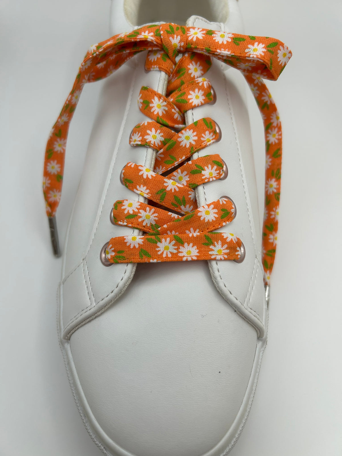 Lacets orange à marguerites blanches noués sur une basket blanche