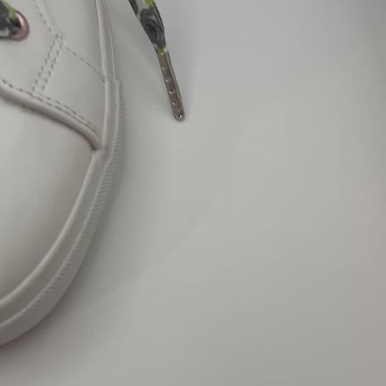 Gros plan sur les lacets blancs à roses noires et feuilles vertes croisés sur une basket blanche 