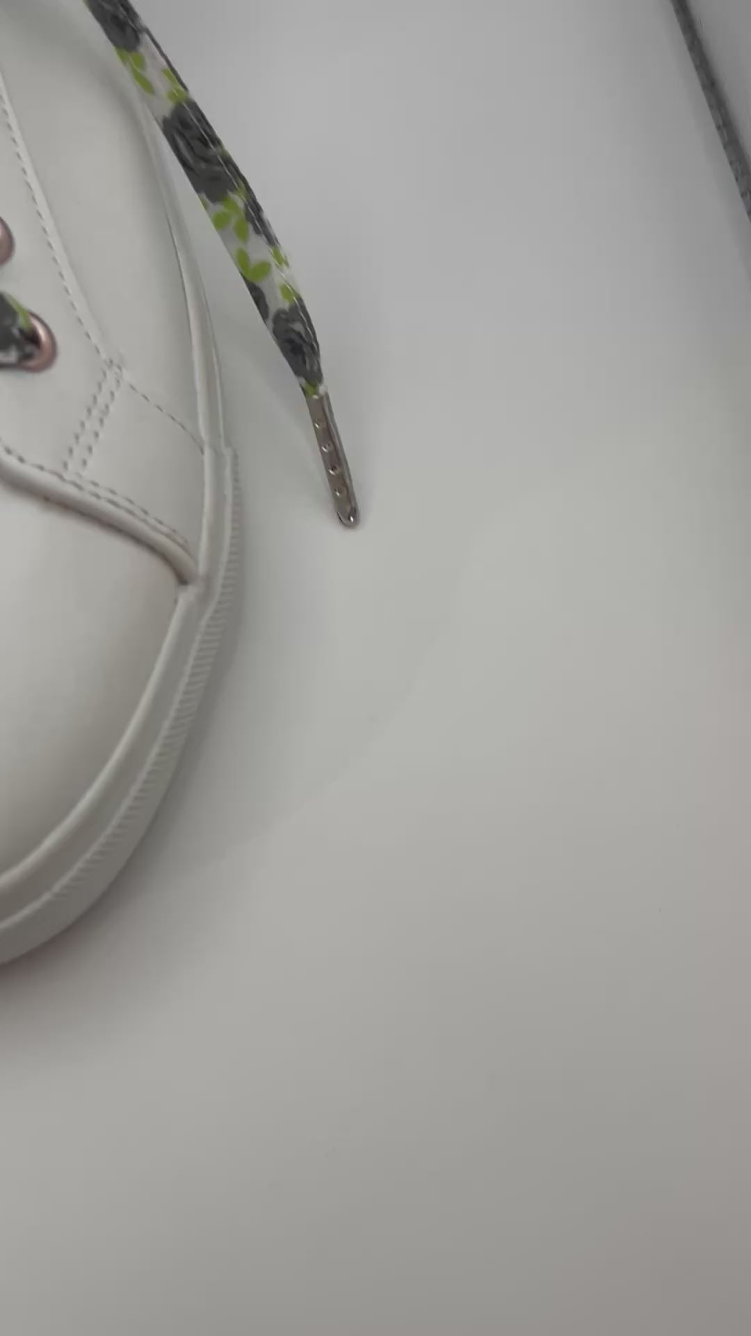Gros plan sur les lacets blancs à roses noires et feuilles vertes croisés sur une basket blanche 